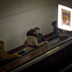 two people speak while riding an up escalator in an underground subway station. A flourescent light with a picture decorating it lights the escalator.